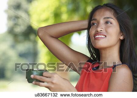 Stock Image - Portrait of young woman holding coffee cup with hand in hair. Fotosearch