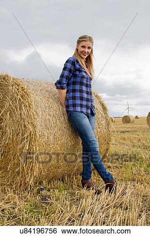 Stock Photograph - Portrait of young woman leaning against straw bale. Fotosearch