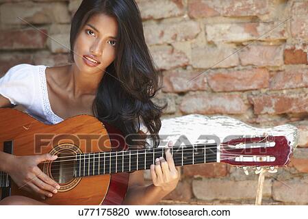 Stock Image - Portrait of young woman playing guitar. Fotosearch