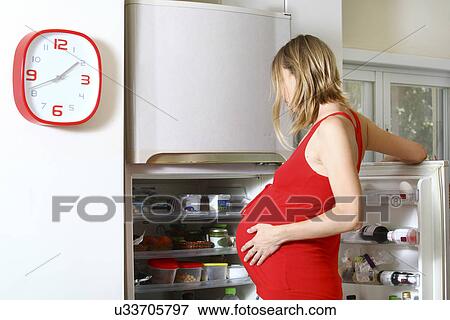 Stock Photo - Pregnant woman with craving looking in fridge. Fotosearch