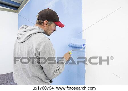 Picture - Rear view of man painting wall blue. Fotosearch