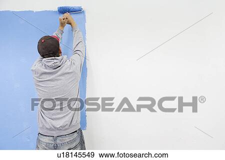 Stock Photo - Rear view of man painting wall blue. Fotosearch