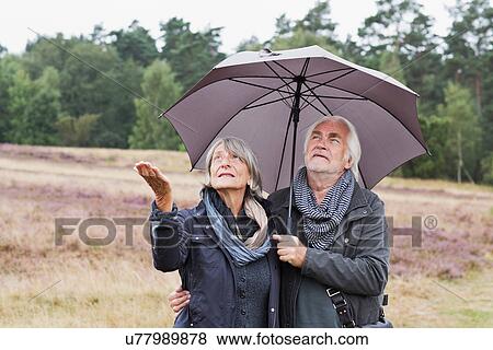 Stock Photo - Senior couple under umbrella checking for rain. Fotosearch