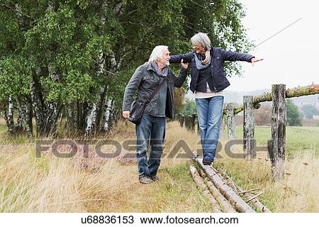 Stock Image - Senior couple, woman balancing on logs. Fotosearch