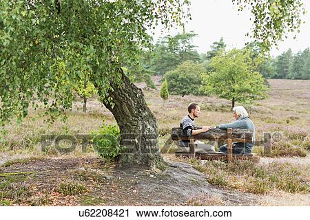 Stock Image - Senior man and mid adult man sitting on bench. Fotosearch