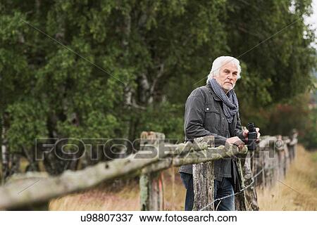Senior man leaning on wooden fence with binoculars View Large Photo Image Stock Photo - Senior man leaning on wooden fence with binoculars. Fotosearch