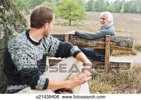 Senior man sitting on bench talking to mid adult man View Large Photo Image Stock Photograph - Senior man sitting on bench talking to mid adult man. Fotosearch