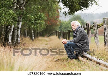 Stock Image - Senior man sitting on log. Fotosearch