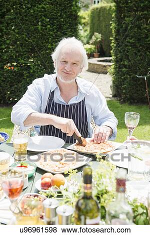 Senior man wearing apron cutting pizza View Large Photo Image Stock Photo - Senior man wearing apron cutting pizza. Fotosearch