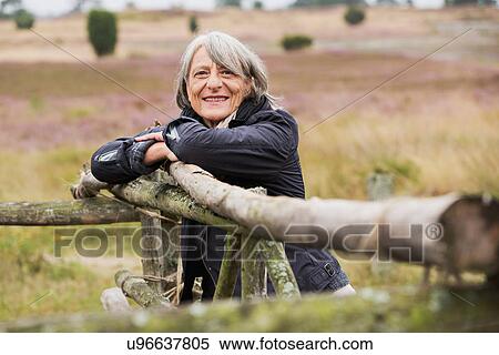 Senior woman leaning on wooden fence smiling towards camera View Large Photo Image Stock Photography - Senior woman leaning on wooden fence smiling towards camera. Fotosearch