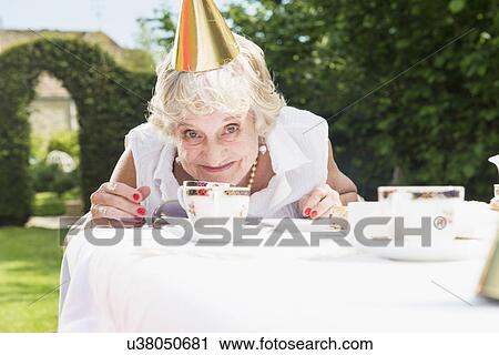 Stock Image - Senior woman wearing party hat looking at camera, smiling. Fotosearch