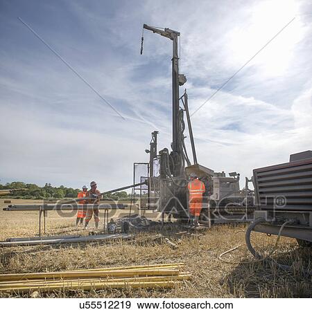 Stock Photo - Small team of workers operating drilling rig in field. Fotosearch