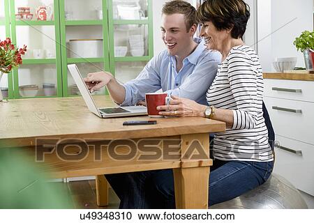 Stock Image - Son teaching mother to use laptop. Fotosearch