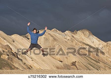 Stock Image - Teenage boy jumping in front of mountain range, Landmannalaugar, Fjallabak, Iceland. Fotosearch