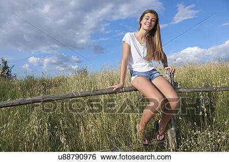 Stock Photograph - Teenage girl sitting on wooden fence, Tuscany, Italy. Fotosearch