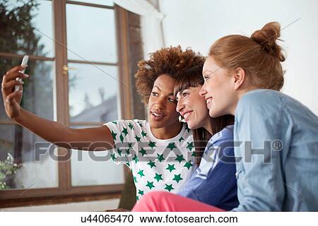 Three female friends photographing themselves with camera phone View Large Photo Image Stock Image - Three female friends photographing themselves with camera phone. Fotosearch