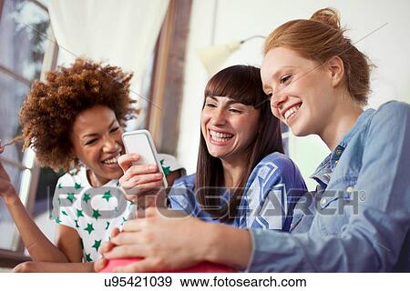 Stock Photo - Three female friends using smartphone. Fotosearch