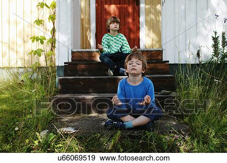 Stock Photo - Two boys sitting cross legged on steps meditating. Fotosearch