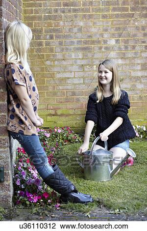 Two girls in garden watering flower bed View Large Photo Image Stock Image - Two girls in garden watering flower bed. Fotosearch