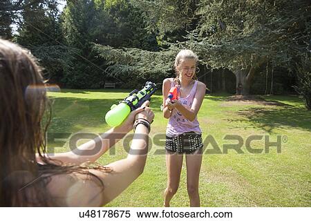 Stock Photography - Two teenage girls firing water guns in garden. Fotosearch