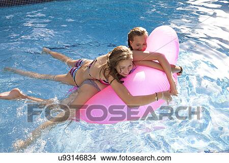Two teenage girls holding onto air bed in swimming pool View Large Photo Image Picture - Two teenage girls holding onto air bed in swimming pool. Fotosearch