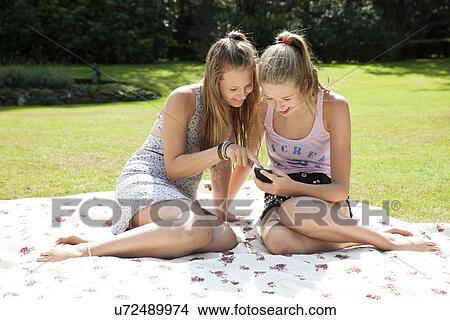 Two teenage girls on picnic blanket looking at mobile phone View Large Photo Image Picture - Two teenage girls on picnic blanket looking at mobile phone. Fotosearch