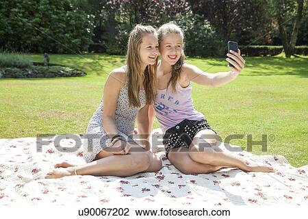 Two teenage girls on picnic blanket taking self portrait View Large Photo Image Stock Image - Two teenage girls on picnic blanket taking self portrait. Fotosearch