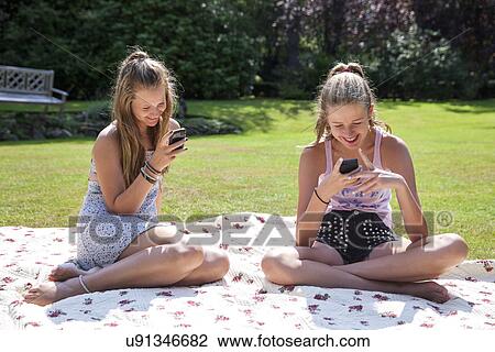 Two teenage girls on picnic blanket looking at mobile phones View Large Photo Image Stock Image - Two teenage girls on picnic blanket looking at mobile phones. Fotosearch