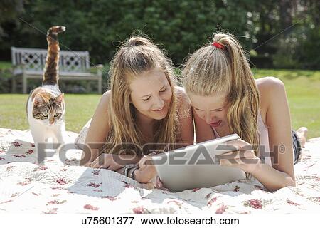 Stock Photo - Two teenage girls on picnic blanket looking at digital tablet. Fotosearch