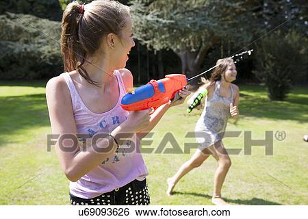 Two teenage girls playing with water guns in garden View Large Photo Image Stock Photograph - Two teenage girls playing with water guns in garden. Fotosearch