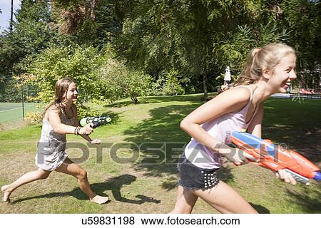 Two teenage girls running with water guns in garden View Large Photo Image Stock Photo - Two teenage girls running with water guns in garden. Fotosearch