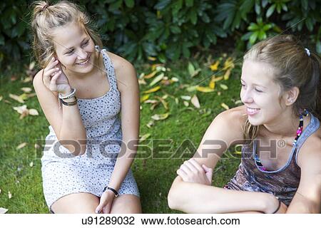 Stock Image - Two teenage girls sitting in garden. Fotosearch