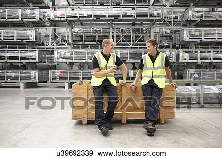 Two warehouse workers leaning on crate in engineering warehouse View Large Photo Image Stock Photo - Two warehouse workers leaning on crate in engineering warehouse. Fotosearch