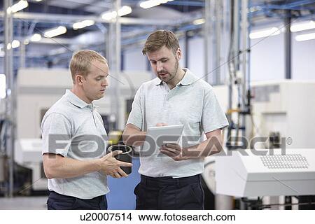 Picture - Two workers looking at digital tablet in engineering warehouse. Fotosearch