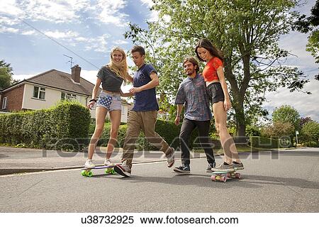 Stock Photography - Two young couples skateboarding on road. Fotosearch