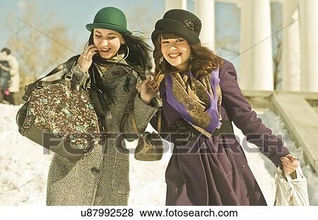 Stock Photo - Two young women carrying bags in snow. Fotosearch
