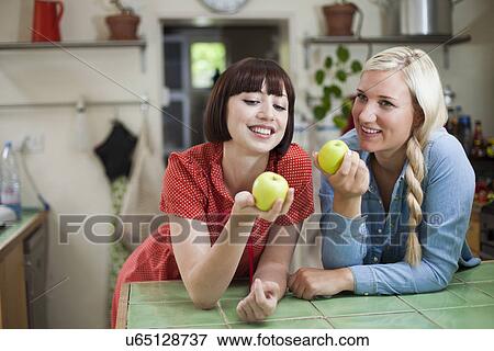 Two young women in kitchen holding apples View Large Photo Image Stock Photo - Two young women in kitchen holding apples. Fotosearch