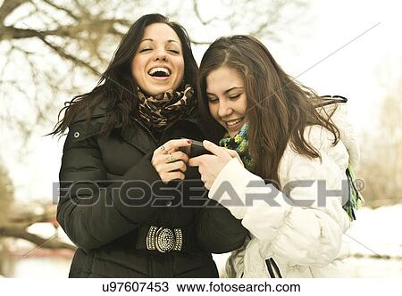 Two young women laughing at mobile phone in park in winter View Large Photo Image Stock Image - Two young women laughing at mobile phone in park in winter. Fotosearch