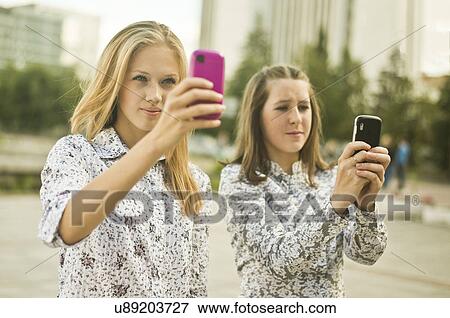Two young women taking self portraits on mobile phone View Large Photo Image Stock Photo - Two young women taking self portraits on mobile phone. Fotosearch