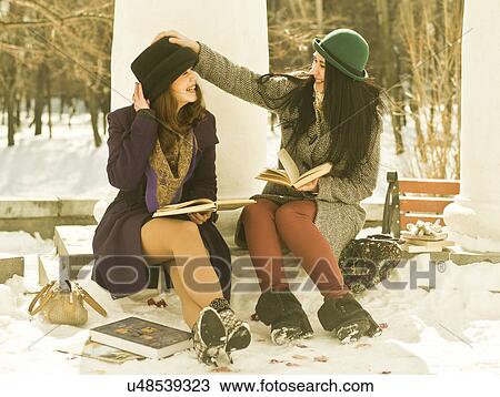 Stock Image - Two young women with books on park bench in snow. Fotosearch