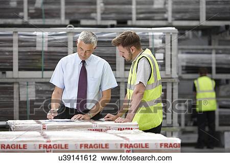 Stock Image - Warehouse worker and manager checking order in engineering warehouse. Fotosearch