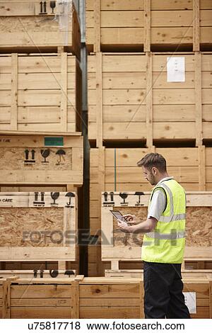 Stock Photo - Warehouse worker checking crates in engineering warehouse. Fotosearch