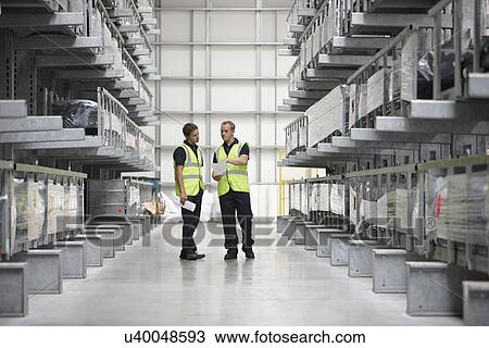 Stock Image - Warehouse workers in engineering warehouse. Fotosearch