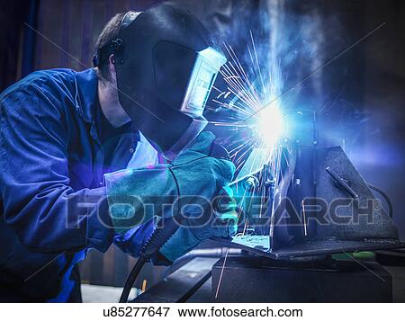 Welder wearing face mask and protective gloves in factory View Large Photo Image Stock Photo - Welder wearing face mask and protective gloves in factory. Fotosearch