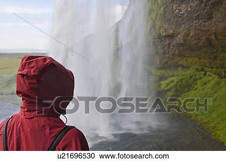 Stock Image - Woman admiring the waterfall Seljalandsfoss in south Iceland. Fotosearch