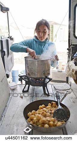 Stock Image - Woman cooking in the back of a van with a large saucepan, Landmannalaugar, Fjallabak, Iceland. Fotosearch