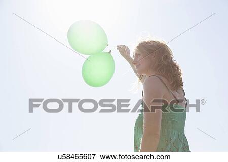 Stock Photo - Woman holding two green balloons, Wales, UK. Fotosearch