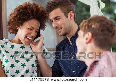 Woman on smartphone laughing with male friends View Large Photo Image Stock Photo - Woman on smartphone laughing with male friends. Fotosearch
