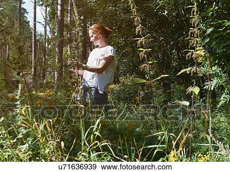 Stock Photo - Woman standing in forest, looking at plants. Fotosearch