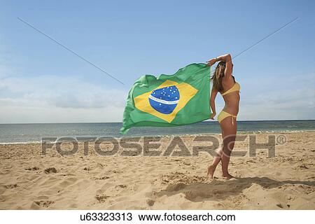 Stock Image - Woman walking on beach with brazilian flag. Fotosearch
